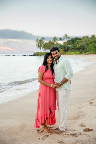 Hawaii Engagement Photographer captures woman wearing pink dress and hugging fiance during sunset beach engagement photos