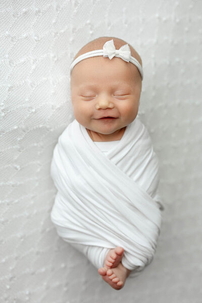 A baby smiles while laying on a white backdrop posed by a Vancouver Photographer