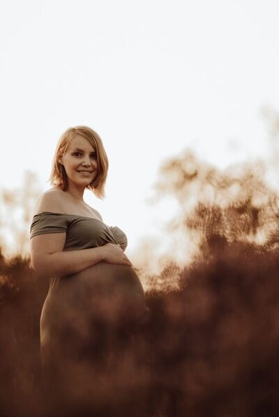 Zwangerschapsshoot vrouw tussen heide bij zonsondergang




