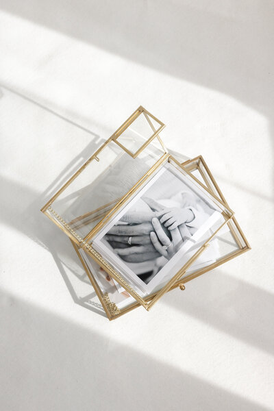 Flat lay of printed black and white photography of family hands in a gold glass keepsake box, showcasing luxury photography artwork by Little Palm Photography Studio in Northern California.