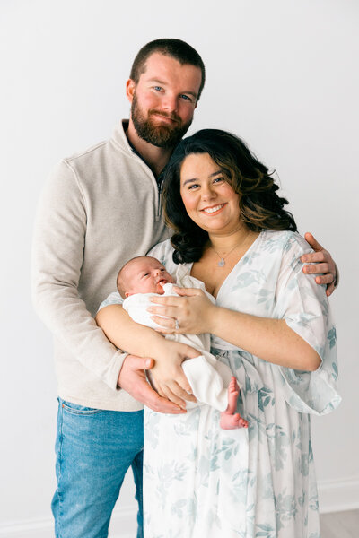 Family poses with their newborn for family portraits at a local Knoxville Studio in front of a white backdrop. 