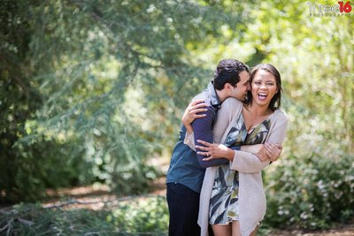 Groom to be whispers in his Bride's ear making her laugh during photo session at The Huntington Library & Gardens in San Marino
