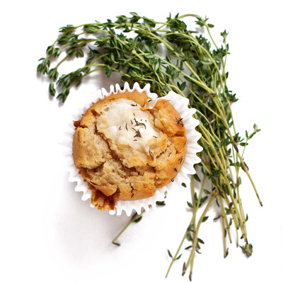 A muffin sits on a white background with thyme around it