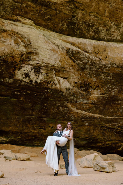 Groom holding bride in his arms at Ash Cave in Hocking Hills State Park in Ohio.