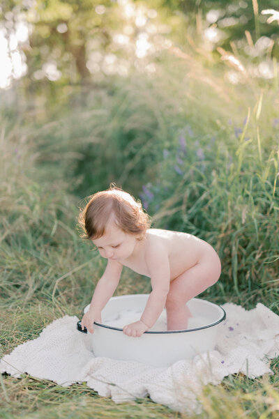 one year old baby girl in a milk bath outside