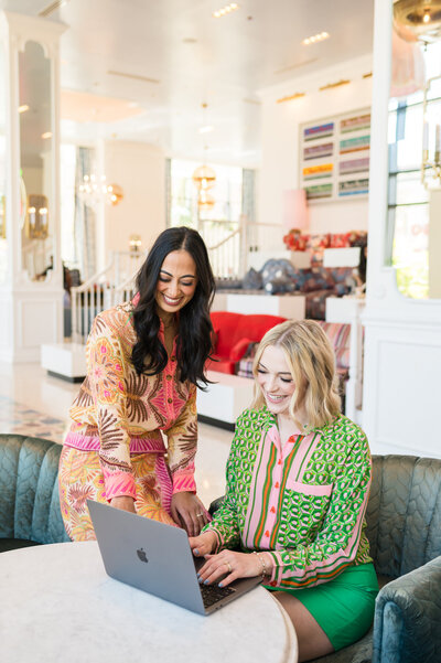 Dr. Brooks and Dr. Templeton, orthodontists in Nashville, TN smiling together in bright colored outfits working with a laptop at a table