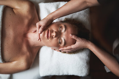 Top view of a peaceful woman receiving a facial massage with gentle pressure applied to her temples and jawline.