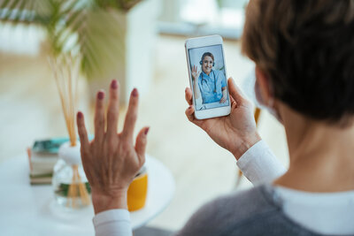 A female doctor waving to a patient on a video call.