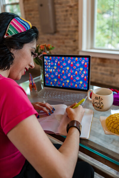 The creative realm of our founder at Soleil Vida Studio, where art workshops for women seeking a GLOW-up come to life. Witness the founder at her glass desk, writing in her agenda, with a computer displaying a uniquely crafted digital texture.