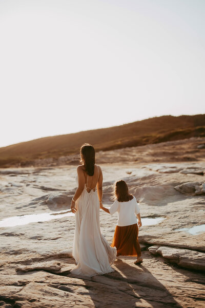 Mohter walking on the beach with her daughter in flowing dress, photographed by Sydney maternity photographer Sophie Lea.
