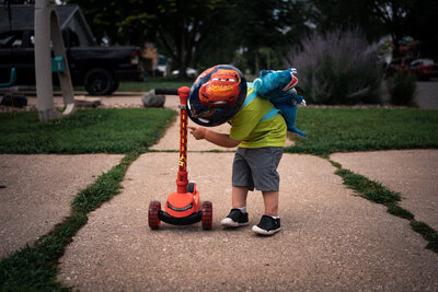 Toddler boy with dinosaur backpack and Lightening McQueen scooter