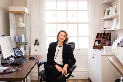 Dr Rebecca Lewis sits in her room at the menopause clinic in Stratford and smiles at the camera for her brand photos