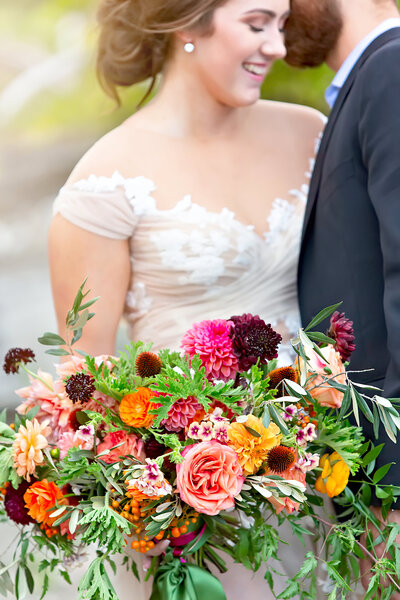 A couple with a smiling bride holding a colorful bouquet.