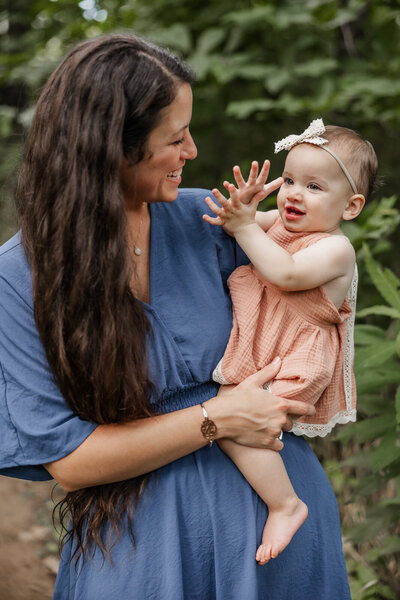 Portrait of a mother holding and smiling at her baby who is clapping and smiling in Bonne Terre, Missouri. 