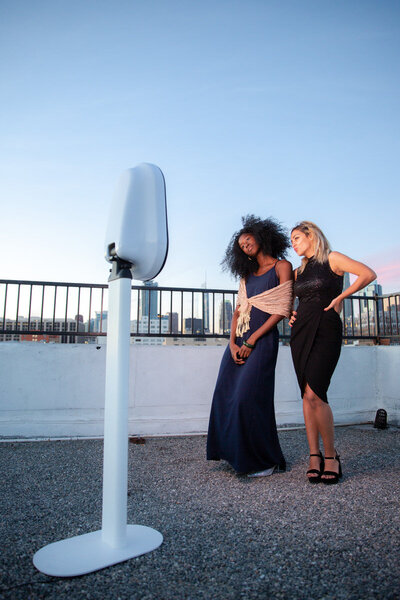 Two women using a photobooth on a city rooftop.