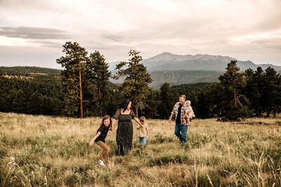 Family walking through wispy mountain grass in Colorado with Pikes Peak, America's Mountain in the background. 