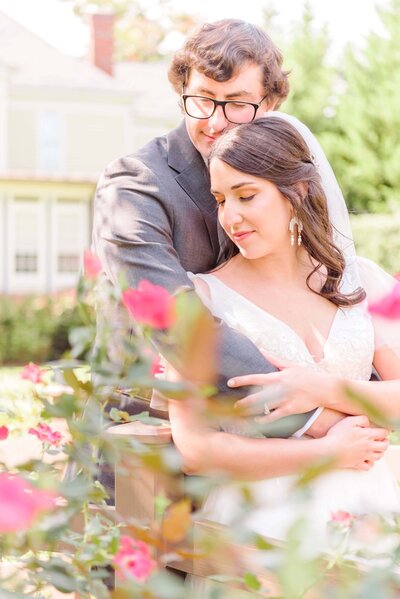 Natalie and Tommy hold each other behind some pink roses.