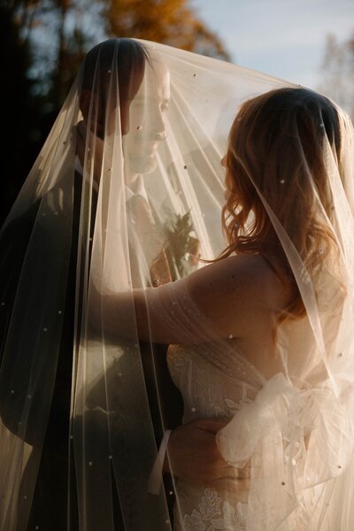A newlywed couple standing together under a veil 
