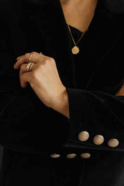 detail ruky ženy v černém kostýmku, ruka se zlatými prstýnky