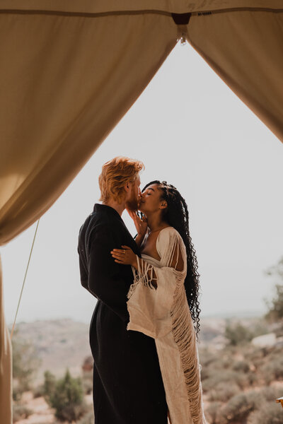 Couple kisses in the doorway of a glamping tent at under canvas during a Moab destination elopement