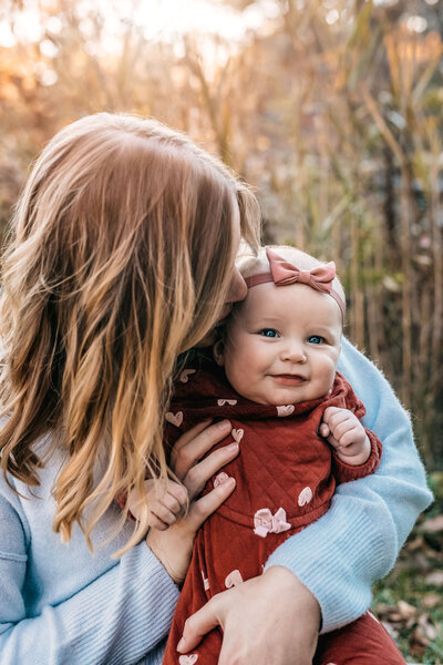Happy baby smiling while mom kiss the side of her head during fall engagement session at the audubon in Auburn NH by Lisa Smith Photography