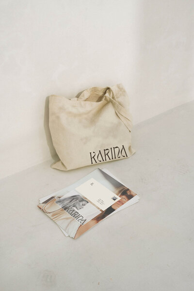 Karina Canva brand kit and Showit website template for wellness coaches, featuring printed overview with color palette and typography, styled with a linen tote on minimal concrete floor.