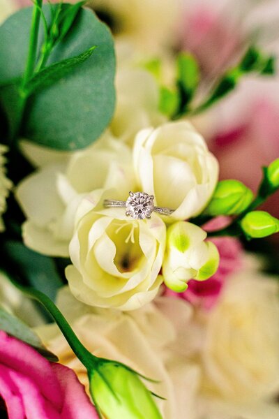 A diamond engagement ring sitting inside a bouquet of ivory and pink flowers from a Catholic wedding photographer