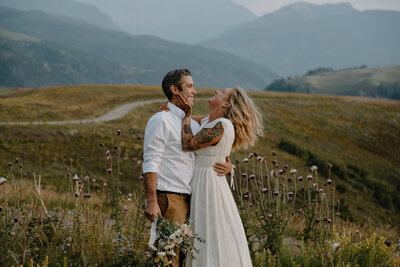 bride and groom feeding each other cake while standing outside with mountains in the background