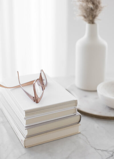 social squares image of a stack of books with glasses at the top and a white backdrop