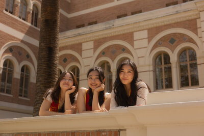 Three girls posing in front of Doheny Library at USC while wearing graduation sashes