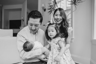 A parent holding a newborn as their partner and other child stand next to them 