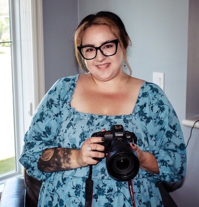 Woman in a blue floral, flowy dress holding a professional camera.