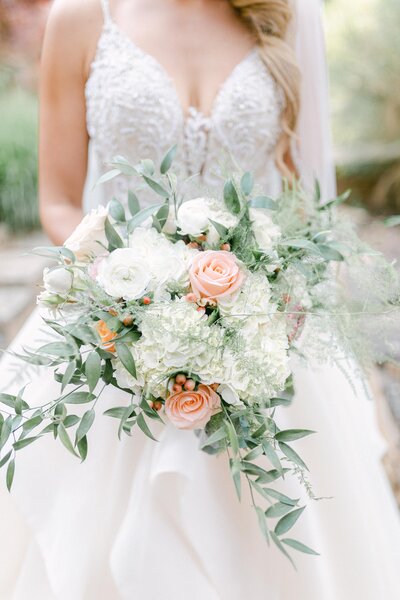 bride holding a peach and white floral bouquet