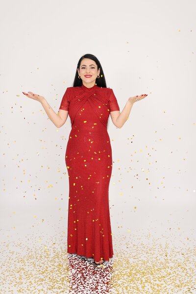 Vancouver boudoir photographer Gina Spanos in a red gown surrounded by gold confetti, celebrating confidence and beauty at her Burnaby studio.