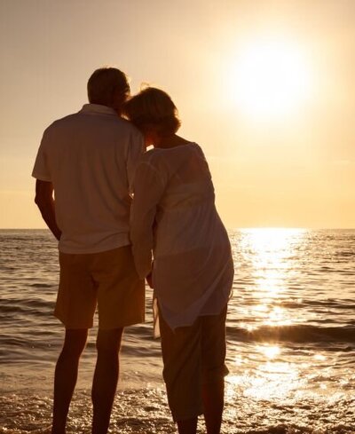 A couple looking into the sunset on the beach while she is leaning on him. They can represent a success story of a couple surviving infidelity with the help of relationship Experts' coaching program. If you are struggling to heal from an affair, apply for our affair recovery program free consultation.