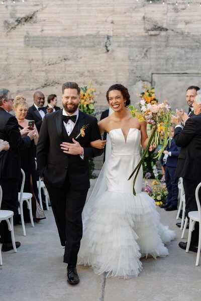 Bride and groom exit wedding ceremony linking arms and smiling
