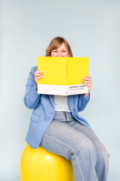 Kat Murphy in a blue blazer holding up a yellow book in front of her face