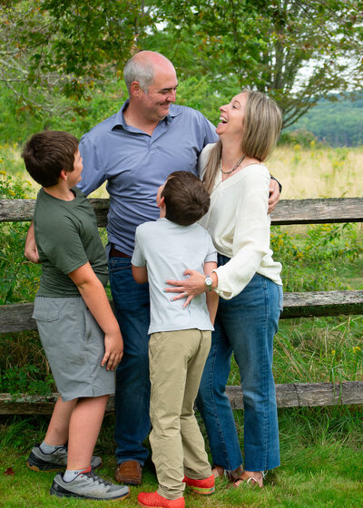 Family of four standing by an old farm fence, looking at each other and smiling. 