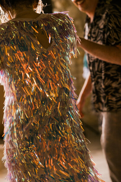 A joyful moment from a wedding in Poland, featuring a guest in a dazzling, iridescent fringe dress dancing under warm, golden light, radiating celebration and movement.