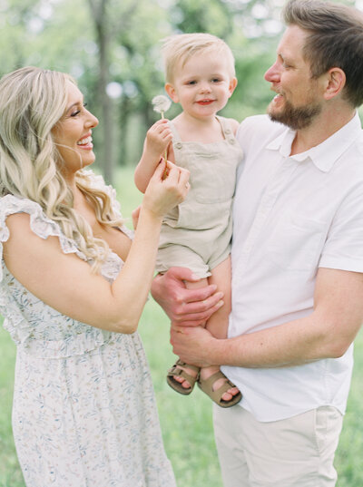 Mother, Toddler and Father smiling together holding a dandelion