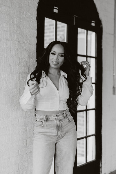 Black and white photo of Tiara in a white top and jeans standing in front of a brick wall