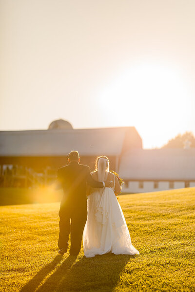 Bride and groom walking away during golden hour to their barn wedding in upstate ny.