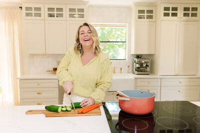 Mollie Mason in a green top smiling while cutting vegetables on a cutting board in her kitchen