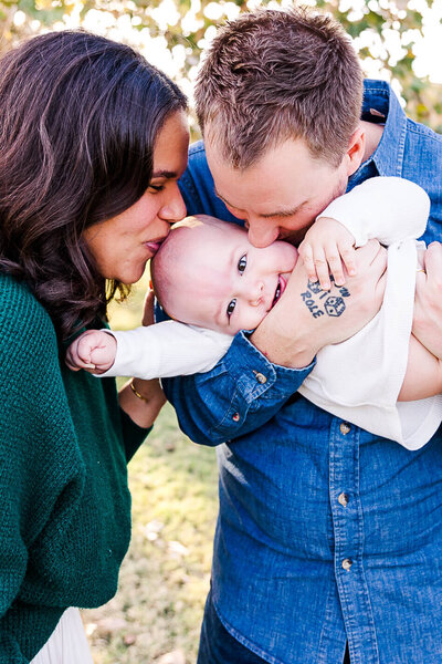 Mum and Dad kissing baby while he smiles at camera.