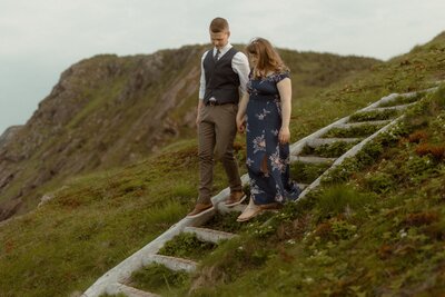 bride and groom walk down wooden steps on the side of a cliff in Newfoundland