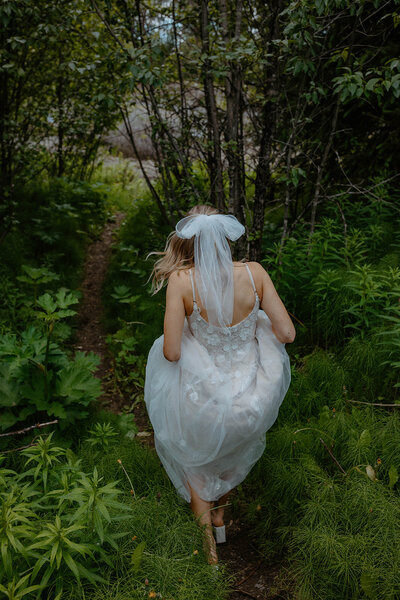 bride walking through the woods as she holds up her dress