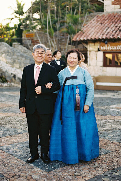 Bride’s parents smiling while walking down the aisle at Altos de Chavón, the mother wearing a traditional Korean hanbok — moment of grace captured by Asia Pimentel Photography.