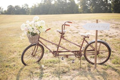 antique bike with a front wicker basket for wedding ceremony filled with flowers in a field coordinated by cait and co events