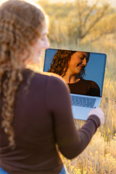 A photo of Haylee's laptop screen reflection. You can see her face as she's smiling with her eyes closed, looking happy and relaxed.