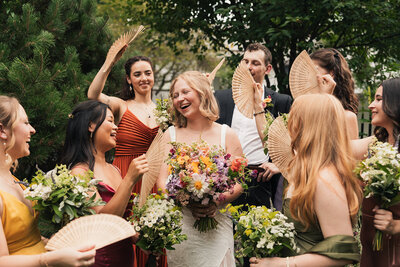 A bride surrounded by her bridemaids in colorful dresses and colorful florals at her backyard wedding in princeton new jersey